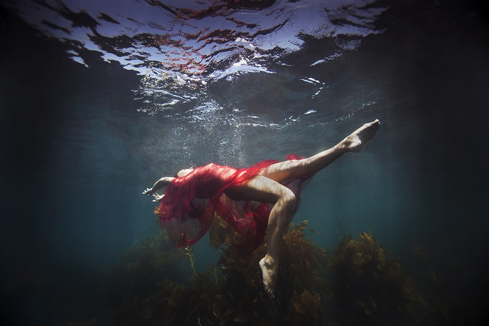 KELSEY WILHM LAYS IN THE OCEAN WITH RED FABRIC. (PHOTOGRAPH BY © JENNY BAUMERT 2013.)