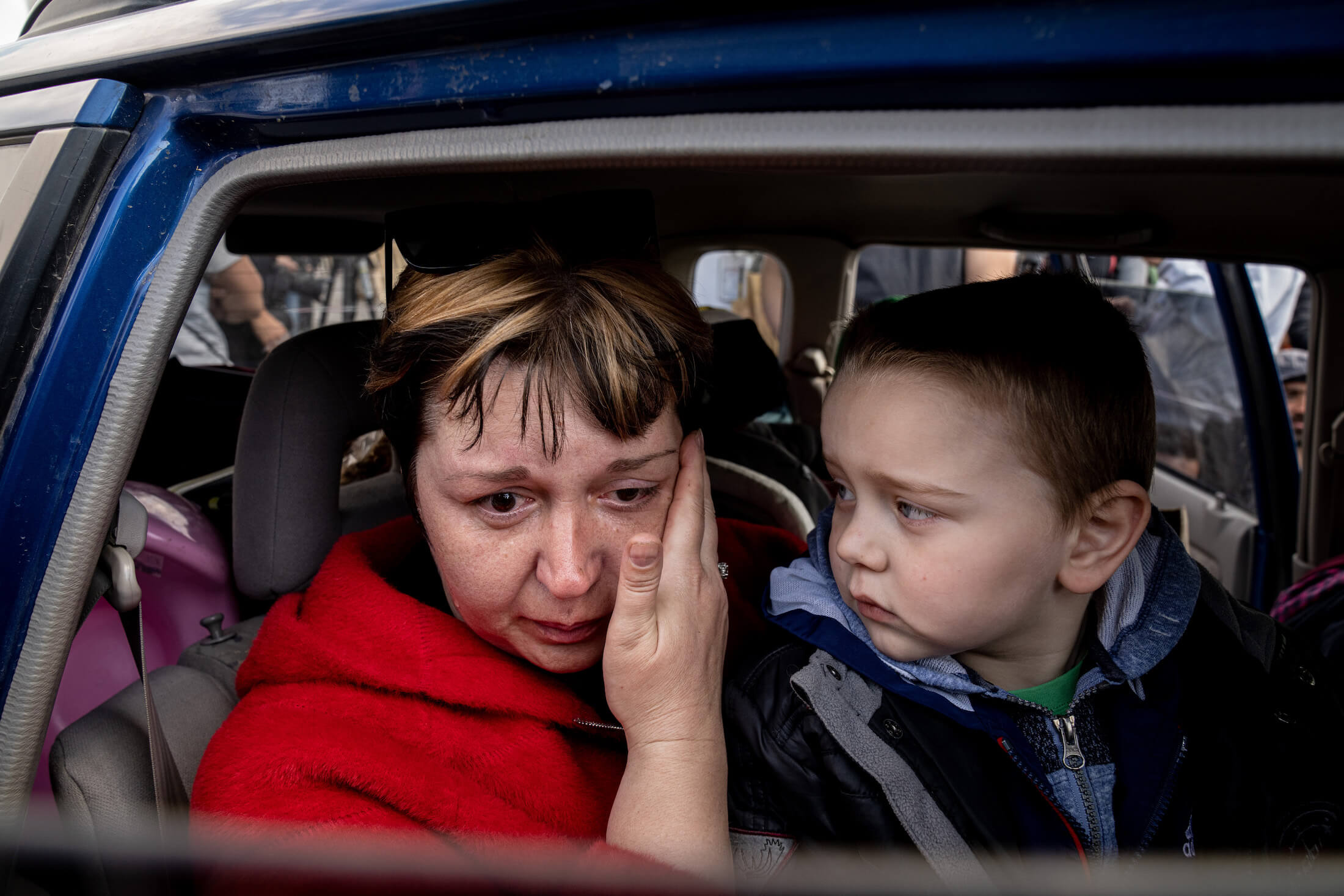 Наталія Потоцька з Василівки з онуком Матвієм плаче в машині в очікуванні на оформлення у пункті прийому переселенців. Запоріжжя, 2 травня 2022 року.